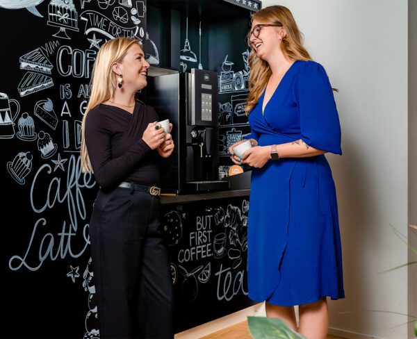 Zijaanzicht twee dames met een kop koffie in gesprek met elkaar